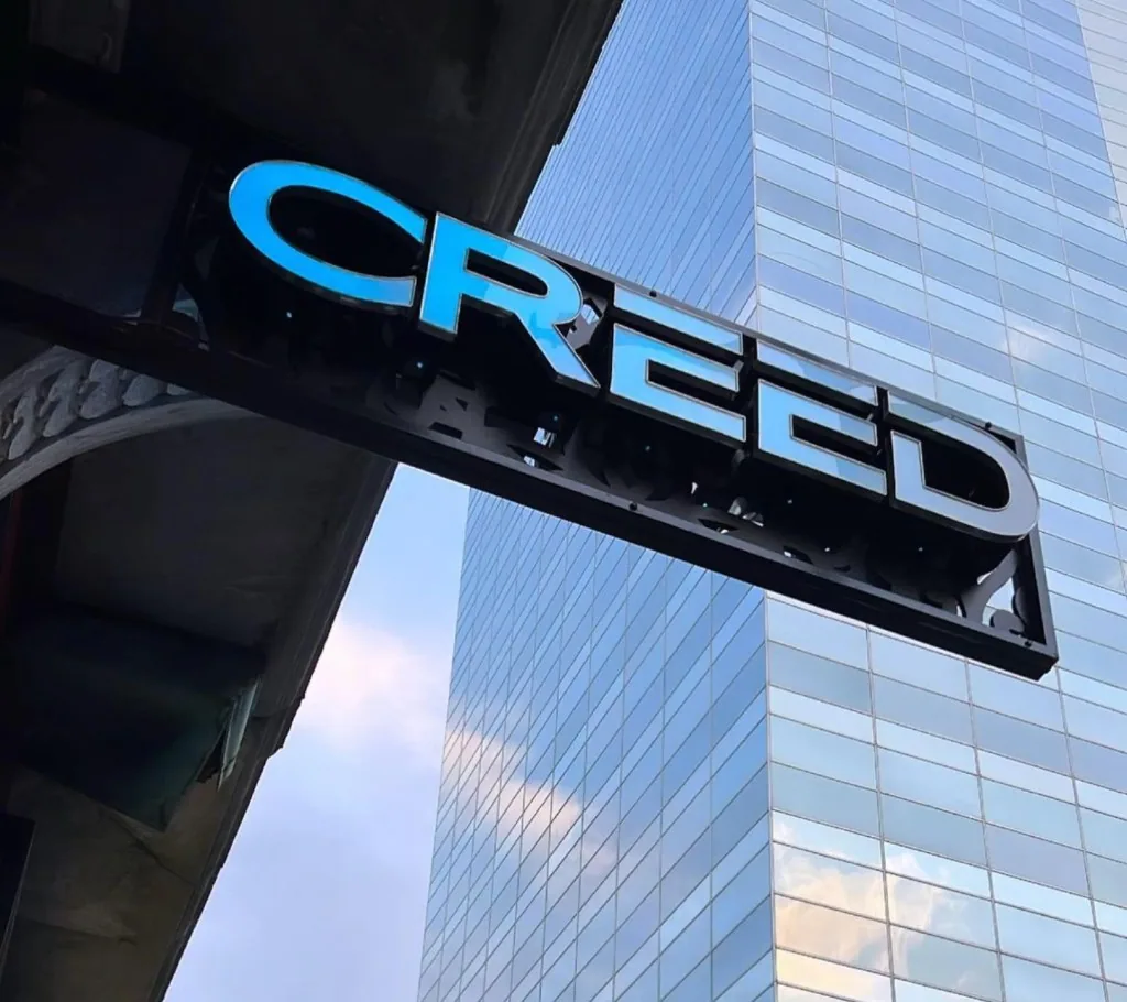 CREED hookah lounge sign against a glass skyscraper at dusk